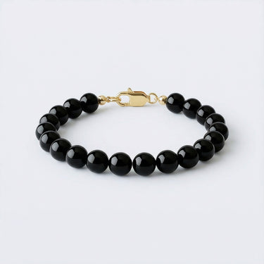 An 8mm Gloss Black Onyx round bead bracelet with a high-polish gold lobster clasp, displayed against a light grey background.
