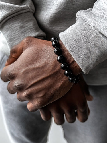 A close-up of a male model's wrist showcasing the bold 8mm scale and high-shine reflective surface of a Gloss Black Onyx bead bracelet.
