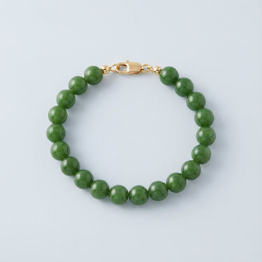 An 8mm green jade round bead bracelet featuring a high-polish gold lobster clasp, displayed against a light grey background.
