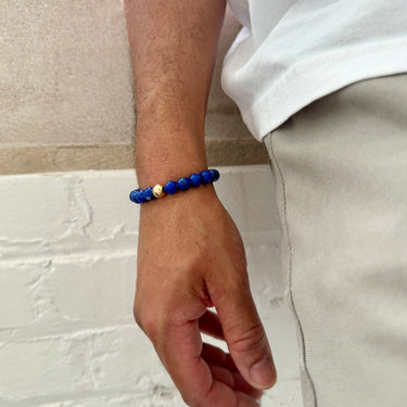 A lifestyle shot of a male model wearing an 8mm Blue Lapis Lazuli bracelet, showcasing its rich pigment and bold profile paired with a white linen shirt.
