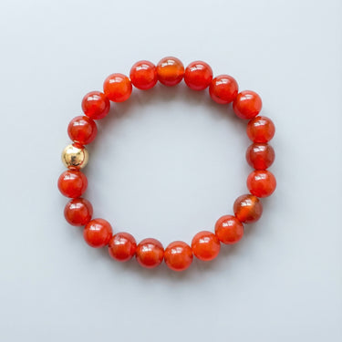 An 8mm Red Agate round bead bracelet featuring a single 14K gold-filled accent bead, highlighting the smooth, polished surface of the gemstones.
