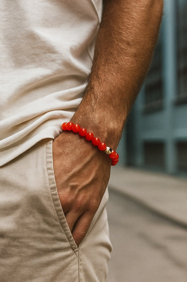 A close-up of a male model's wrist showcasing the bold 8mm scale and warm, translucent red tones of an Agate round bead bracelet paired with khaki trousers.
