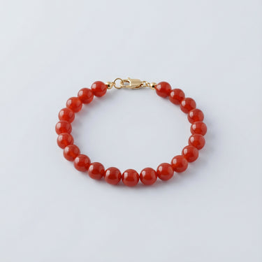 An 8mm Red Agate round bead bracelet with a high-polish gold lobster clasp, highlighting the smooth, polished surface of the gemstones.
