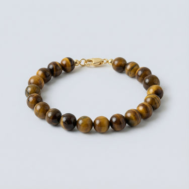 An angled editorial view of an 8mm Tiger's Eye bead bracelet highlighting the smooth, polished surface and gold hardware.

