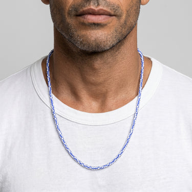 Man wearing a blue and white african chevron glass beaded necklace against a plain background