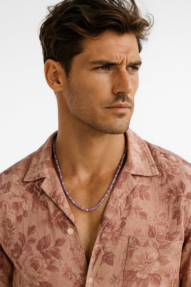 A male model wearing a dusty rose floral print shirt showcasing a purple Amethyst beaded necklace.
