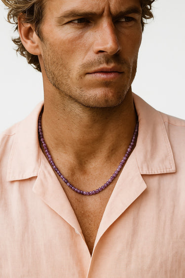 Close-up of a man wearing a peach-colored button-down shirt showcasing a strand of purple Amethyst beads around his neck.

