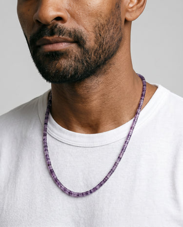 Man wearing a purple amethyst heishi beaded necklace against a neutral background