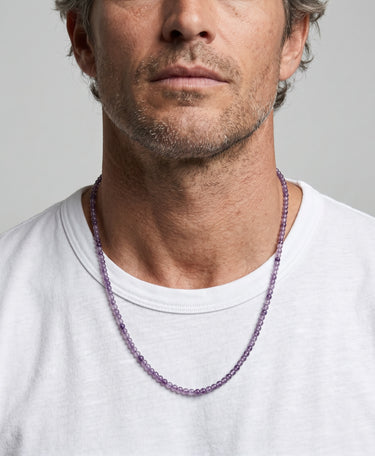 Man wearing a purple amethyst 4mm round beaded necklace against a plain background