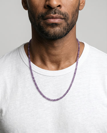 Man wearing a purple amethyst beaded necklace against a plain background