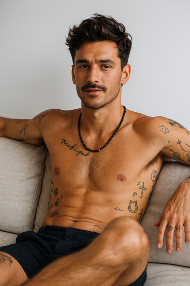 A shirtless male model showcasing the drape and asymmetric gold accent of a matte black onyx necklace.
