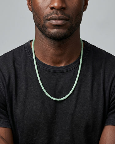 Man wearing a black t-shirt with a light green aventurine heishi necklace.