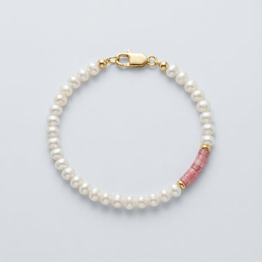 An angled editorial view of a pearl and rhodonite heishi bracelet, highlighting the organic texture of the stones and polished gold hardware.

