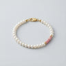 A mixed-media bracelet featuring white baroque pearls, pink petrified rhodonite heishi beads, and 14K gold-filled accents with a gold lobster clasp.

