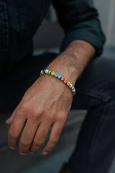 A lifestyle shot of a male model wearing a colorful 6mm Millefiori glass bracelet, highlighting its slim profile and artistic detail.
