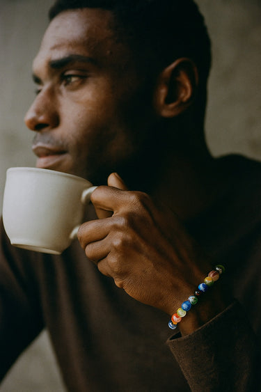 A male model wearing the colorful 8mm Millefiori glass bracelet while holding a coffee cup, highlighting its everyday versatility.
