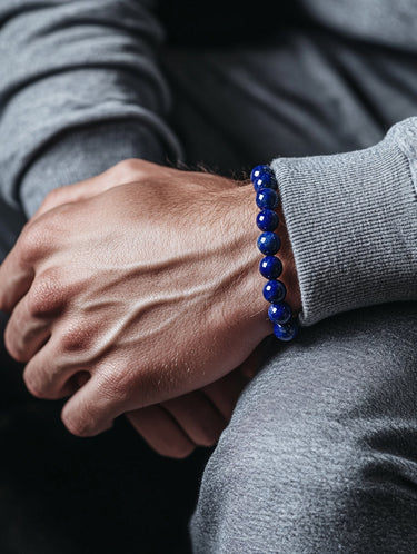 A male model wearing a deep blue Lapis Lazuli bead bracelet, demonstrating its versatility with a textured grey sweatshirt.
