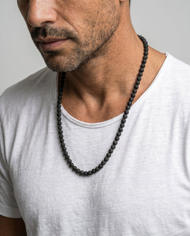 Man wearing a 6mm black lava round rugged beaded necklace against a neutral background