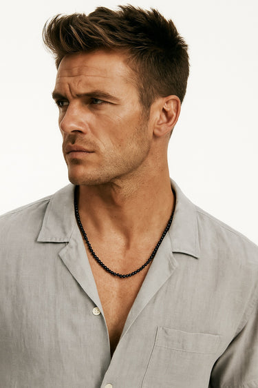 A male model in a light grey linen shirt wearing a single strand of 4mm black onyx gemstone beads.
