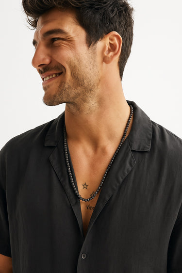 A smiling man in a black open-collar shirt wearing a single strand of 6mm high-gloss black onyx beads.
