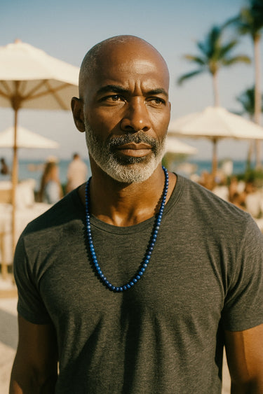 A male model wearing a dark grey linen shirt highlighting the rich saturation of a 6mm Lapis Lazuli necklace.
