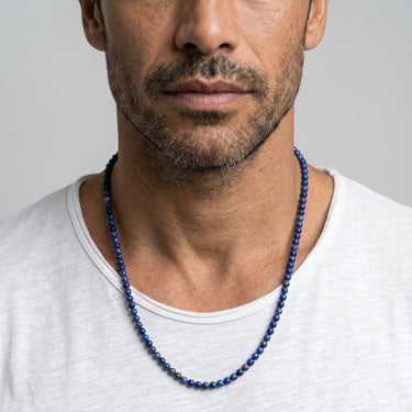 Man wearing a blue lapis lazuli 4mm round beaded necklace against a plain background 