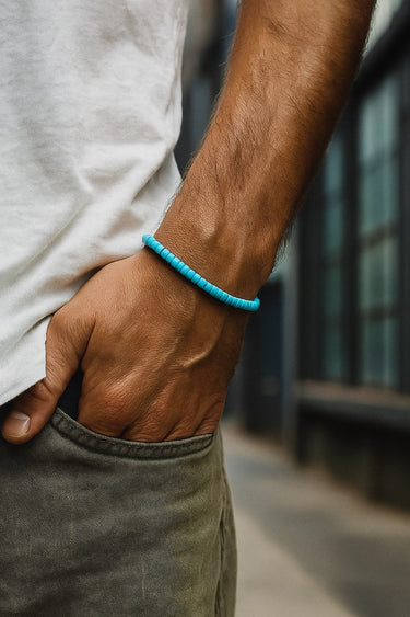 A close-up of a male model's wrist showcasing the vibrant blue tones of a 4mm turquoise heishi bracelet against a white linen shirt.
