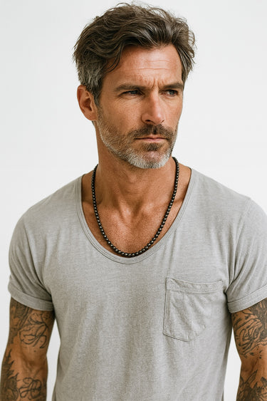 A portrait of a male model in a white t-shirt highlighting the clean, non-reflective texture of a 6mm matte onyx necklace.
