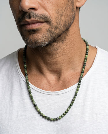 A male model wearing a neutral t-shirt showcasing a single necklace of 6mm round green Chrome Diopside beads.