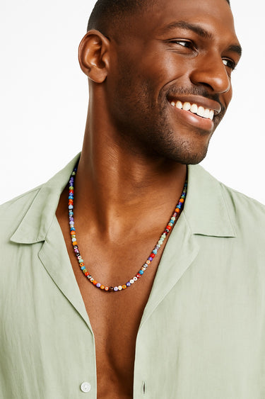 A portrait of a smiling Black male model in a mint green shirt, wearing the colorful Millefiori beaded necklace.
