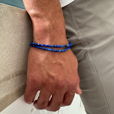A close-up of a male model's wrist showcasing the layered, geometric silhouette and rich blue hues of a double-wrap Lapis Lazuli cube bracelet.
