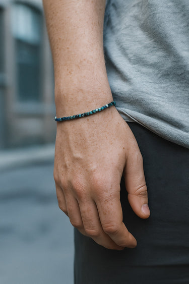 A close-up of a male model's wrist showcasing the sharp geometric silhouette and dark green hues of a 3mm tourmaline cube bracelet.
