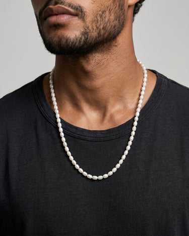 Man wearing a pearl necklace against a neutral background