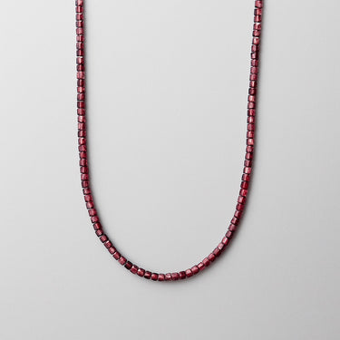 A deep red faceted Garnet cube bead necklace displayed in a U-shape against a light grey background.
