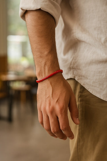 A male model's hand in his pocket, highlighting the low-profile fit and saturated color of a red agate heishi bracelet.
