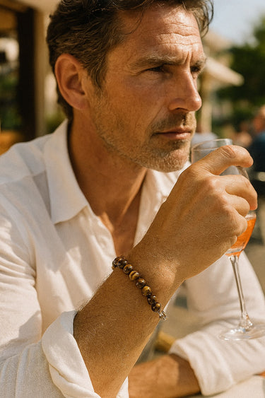 A male model wearing a Tiger's Eye bead bracelet while holding a drink, showcasing its sophisticated, everyday versatility.
