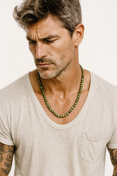 A male model wearing a neutral v-neck shirt showcasing a single strand of 6mm green Chrome Diopside beads.
