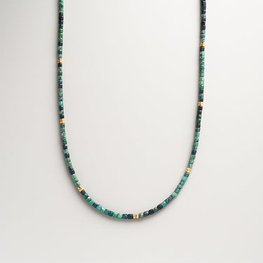 A strand of 2-3mm faceted green and teal tourmaline cube beads with gold spacer beads, displayed in a U-shape against a neutral background.
