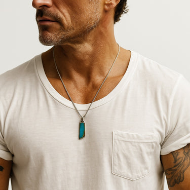 A male model wearing a white crew neck t-shirt highlighting the natural blue tones of a hand-finished turquoise sterling silver pendant.
