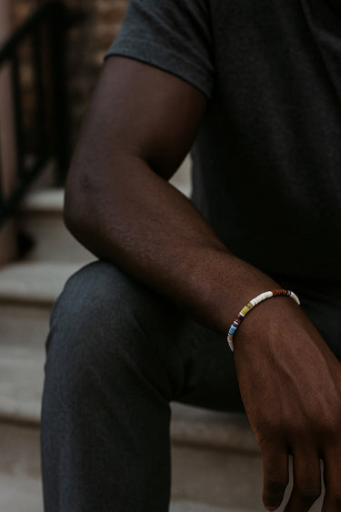 A male model wearing the 4mm multi-gemstone heishi bracelet, highlighting its vibrant natural colors in outdoor lighting.
