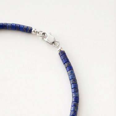 Close-up of heishi lapis beads with round polished sterling silver accent beads and lobster clasp detail on a white background.