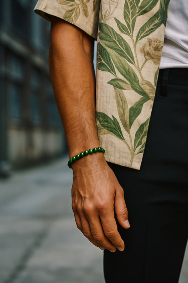 A close-up of a male model's wrist showcasing the bold 8mm scale and vibrant green hues of a jade round bead bracelet paired with a floral print shirt.
