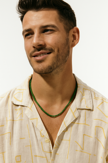 Close-up of a smiling man in a cream patterned button-down shirt wearing a single strand of green jade beads.
