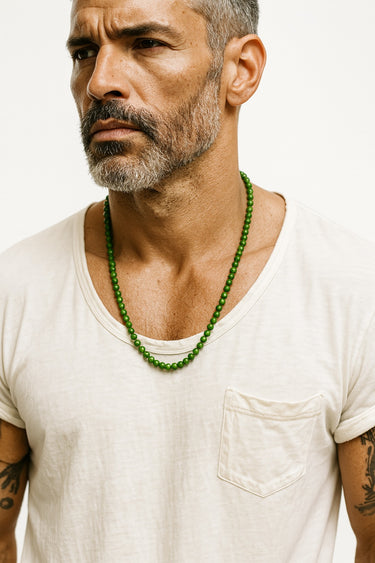 A male model in a white t-shirt highlighting the vibrant, earthy green color of a Nephrite Jade necklace.

