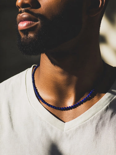 A close-up of a male model wearing a white v-neck shirt showcasing a single strand of 4mm royal blue lapis lazuli beads.
