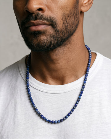 Man wearing a 6mm blue lapis lazuli round beaded necklace against a neutral background