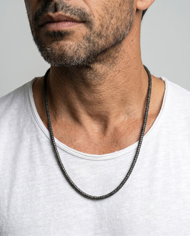 Man wearing a black lava heishi beaded necklace against a gray background