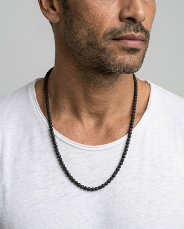 A close-up portrait of a male model in a white t-shirt wearing a single strand of 4mm black rugged lava round beads.