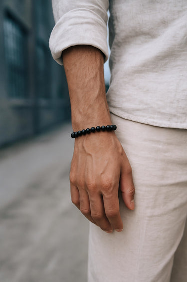 A close-up of a male model's wrist showcasing the bold 8mm scale and velvety matte texture of a black onyx round bead bracelet.
