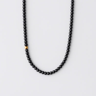 A strand of 4mm matte black onyx beads featuring a single off-centered 14K gold-filled accent bead, displayed in a U-shape.

